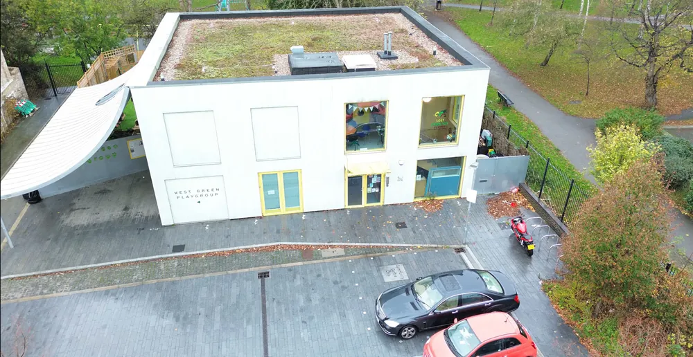 Aerial view of the Goan Community Centre, a white building with yellow framed windows next to the park, with its car park in front