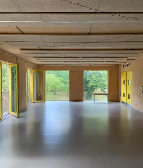The empty main hall with large windows onto trees, wooden walls and yellow doors