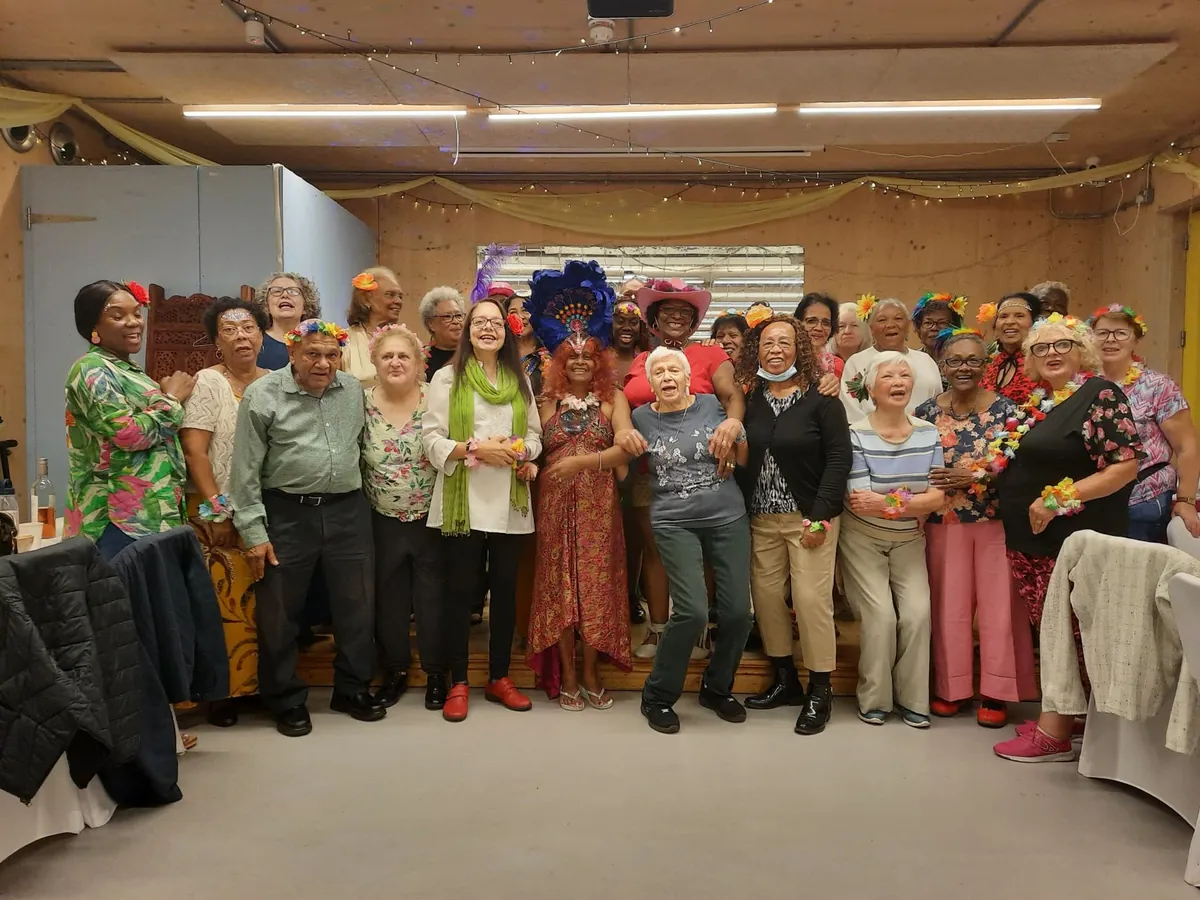 A large group of Centre members in flower garlands and colourful outfits celebrating together in the main hall